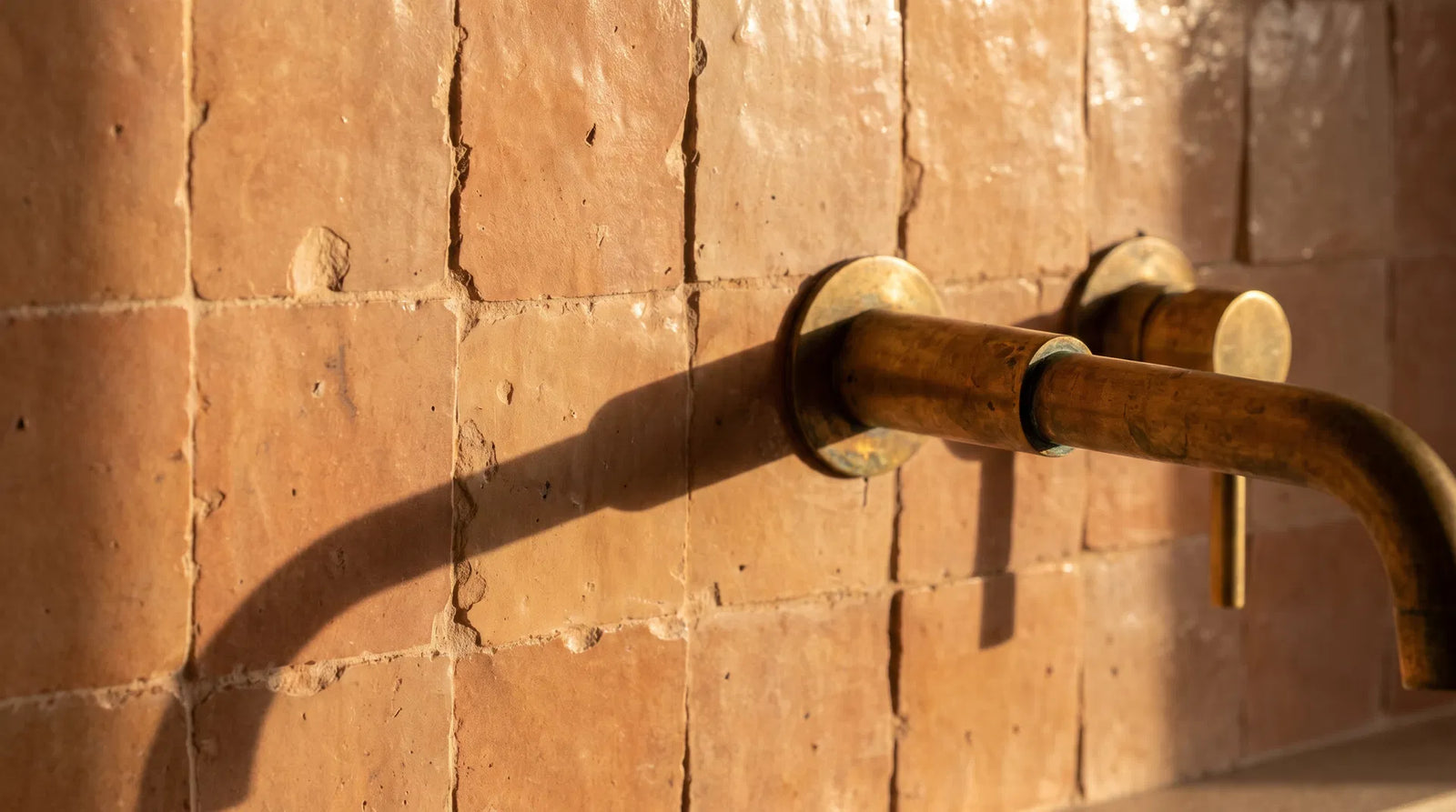 Handmade Moroccan zellige tiles behind an unlacquered brass wall-mounted faucet